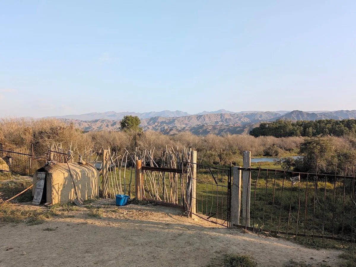 The farm's back gate opening onto the meadow and the river, with mountains beyond