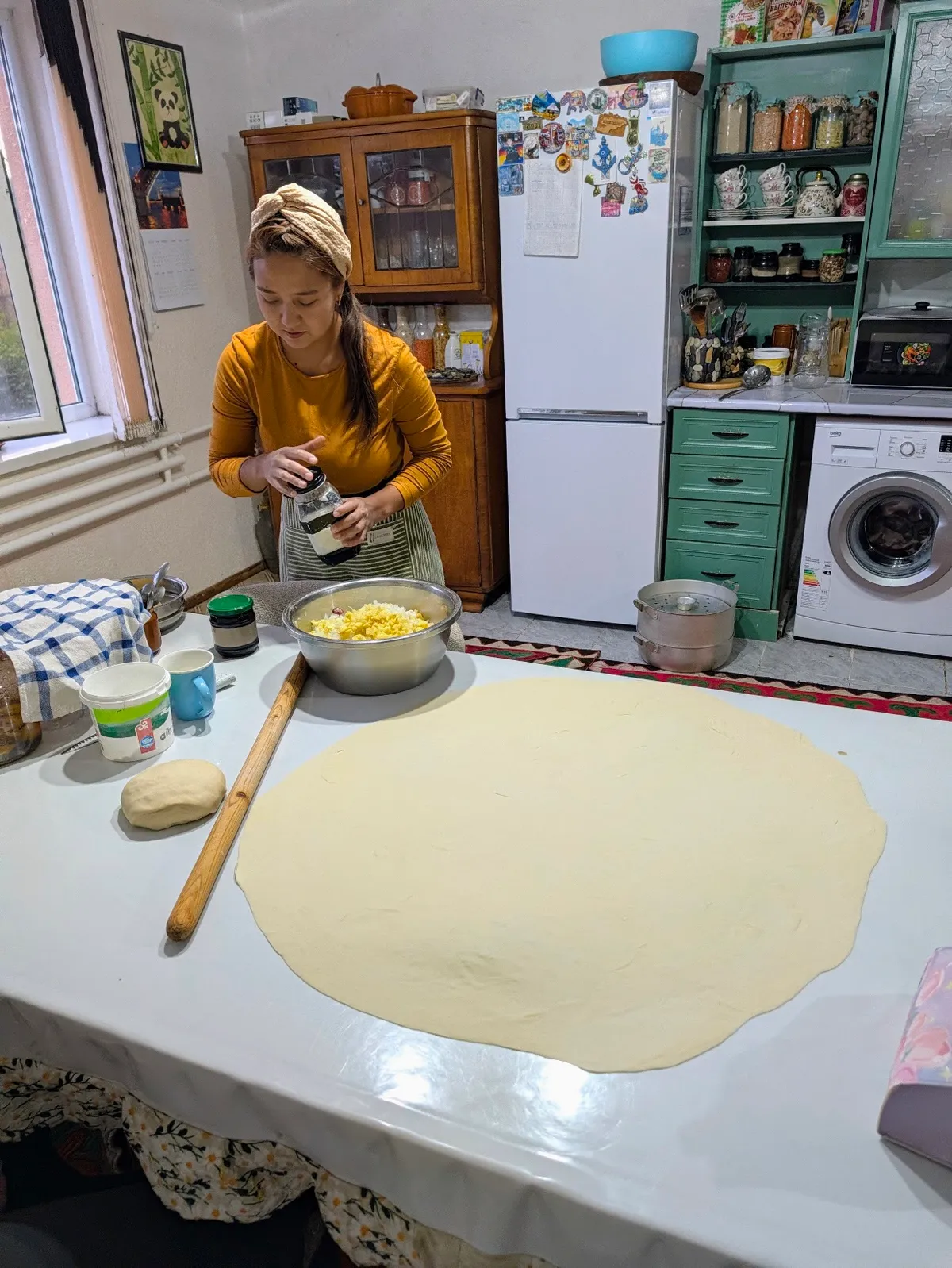 Seasoning the filling beside a big round of rolled-out dough in our kitchen