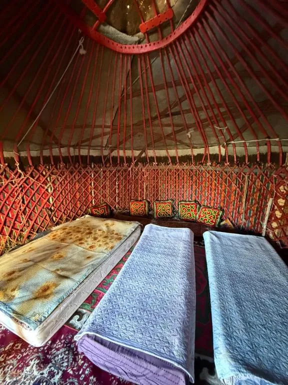 Inside the family yurt, a double bed and two single beds under the red roof poles