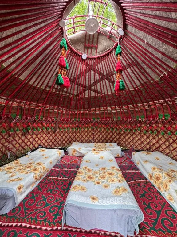 Inside the four-bed yurt, four single beds with sunflower covers under a red roof hung with wool tassels