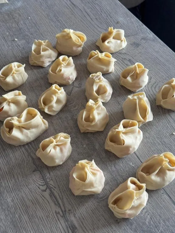 Rows of handmade manty dumplings on a wooden table, ready to steam