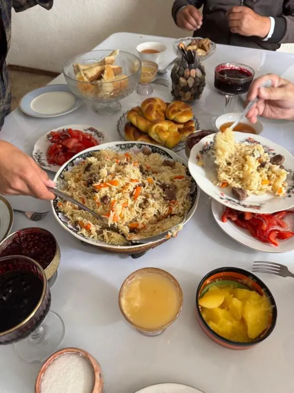 A shared table with plov, bread rolls, salads and homemade jam, with everyone serving themselves