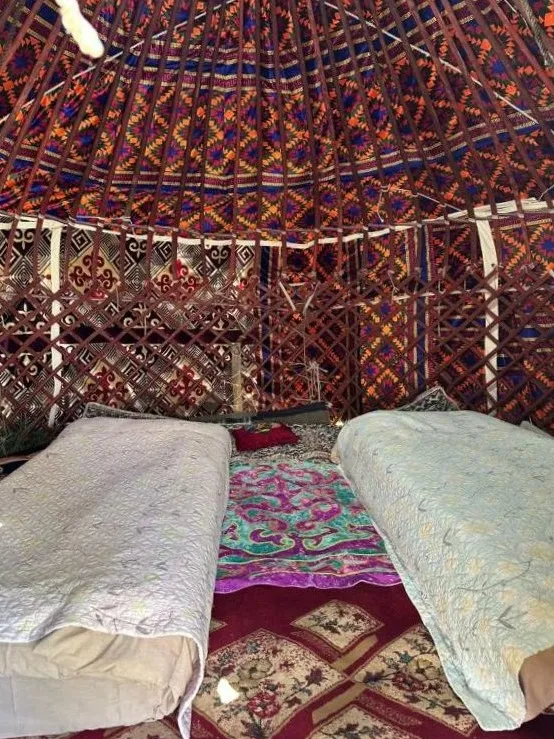 Inside the twin yurt, two single beds on patterned rugs under a patterned roof lining